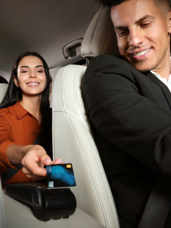 Young woman paying for service using credit card via payment terminal in modern taxi